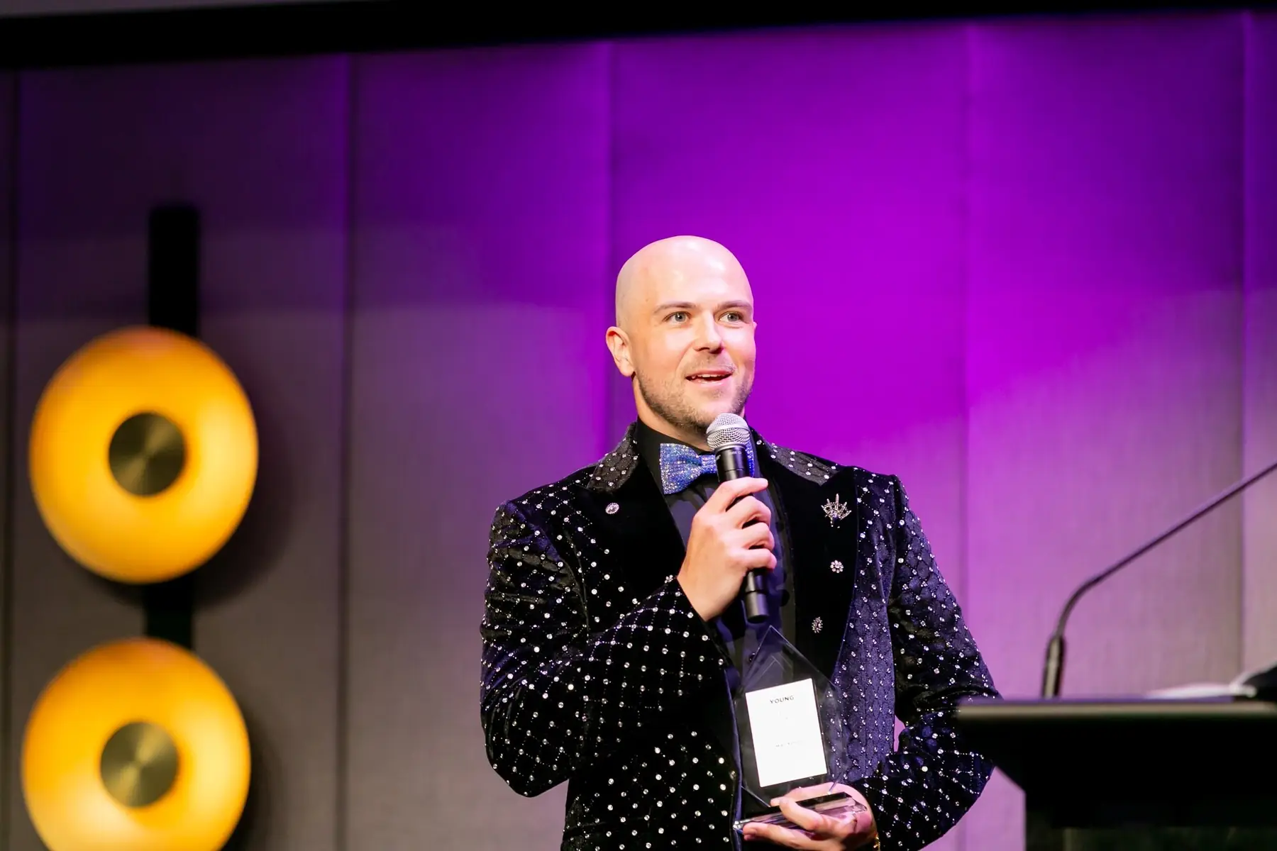 Mike on stage speaking into a microphone, holding an award